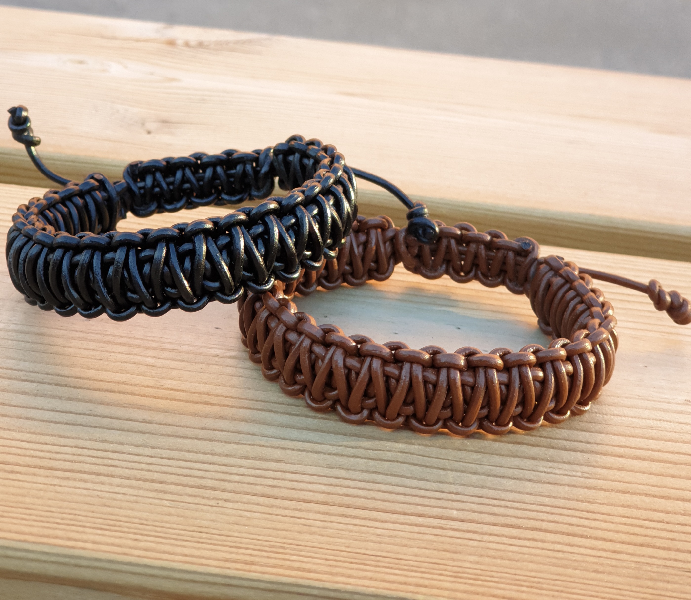 Två flätade bandarmband i svart och brunt, med justerbar knut, placerade på en träyta.