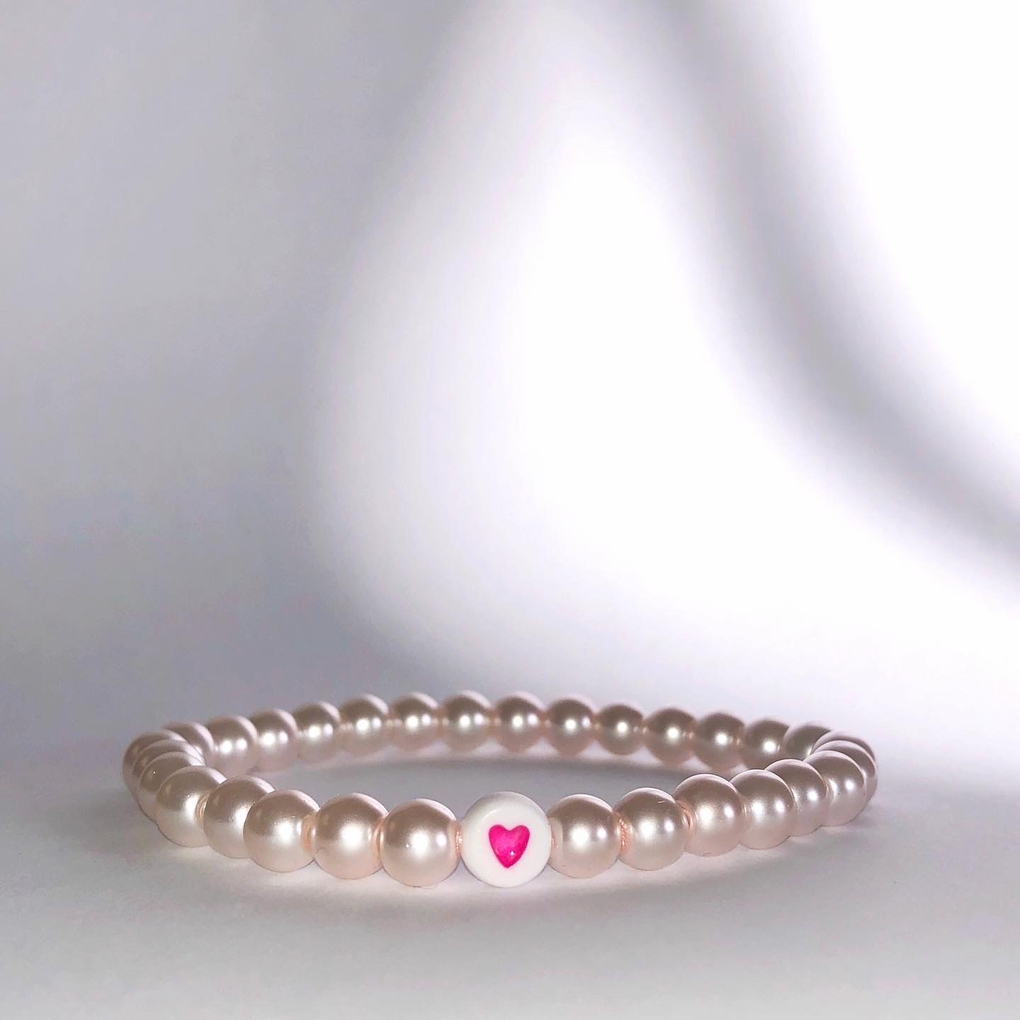 Pärlarmband i pärlvit ton med vit hjärtpärla med rosa hjärta i mitten.